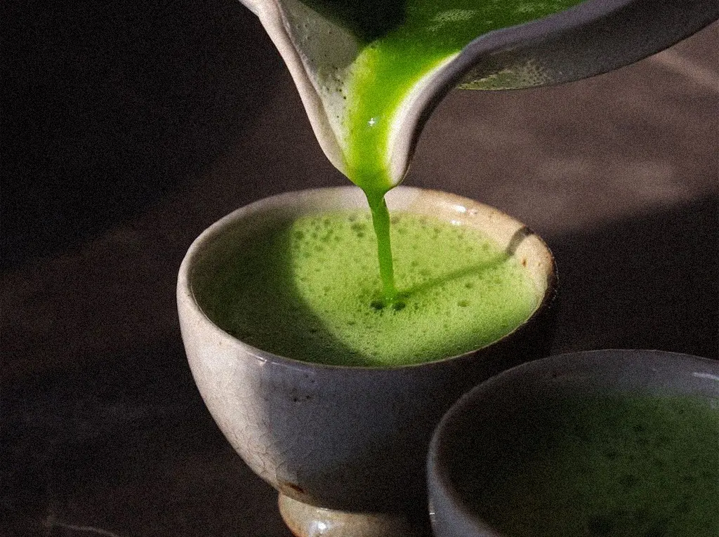 Strumień przygotowanej zielonej herbaty matcha wlewa się do ceramicznej czarki chawan, tworząc gęstą piankę.