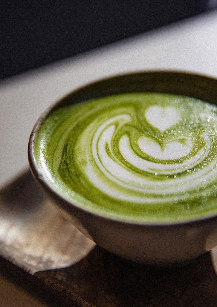 Filiżanka kremowej matcha latte z dekoracyjnym wzorem serca z mlecznej pianki.